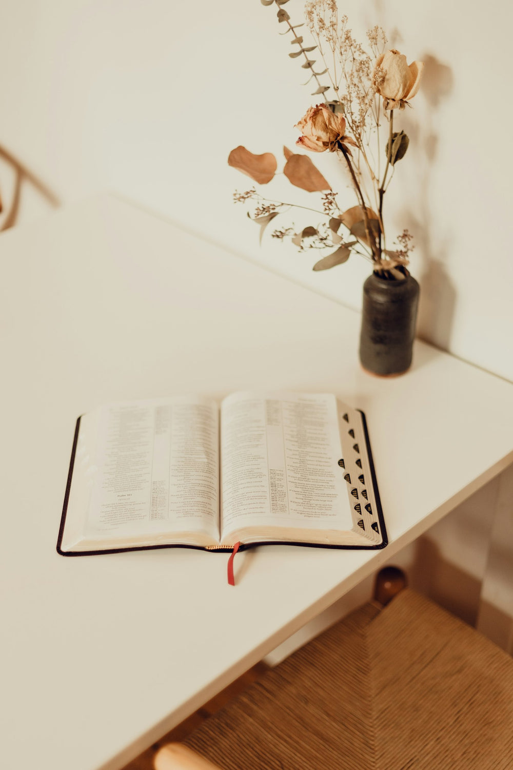 Open Bible on a cream table beside dried flowers in a dark vase